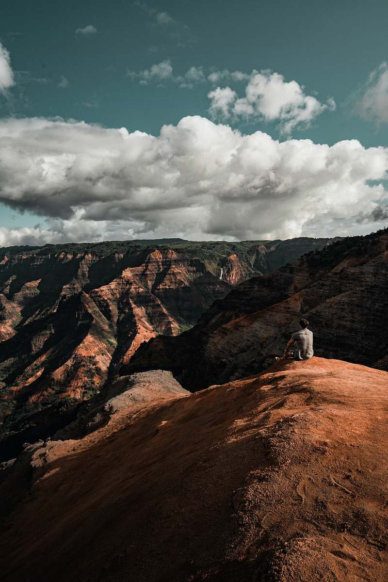 waimea canyon person sitting on mountain cliff grey